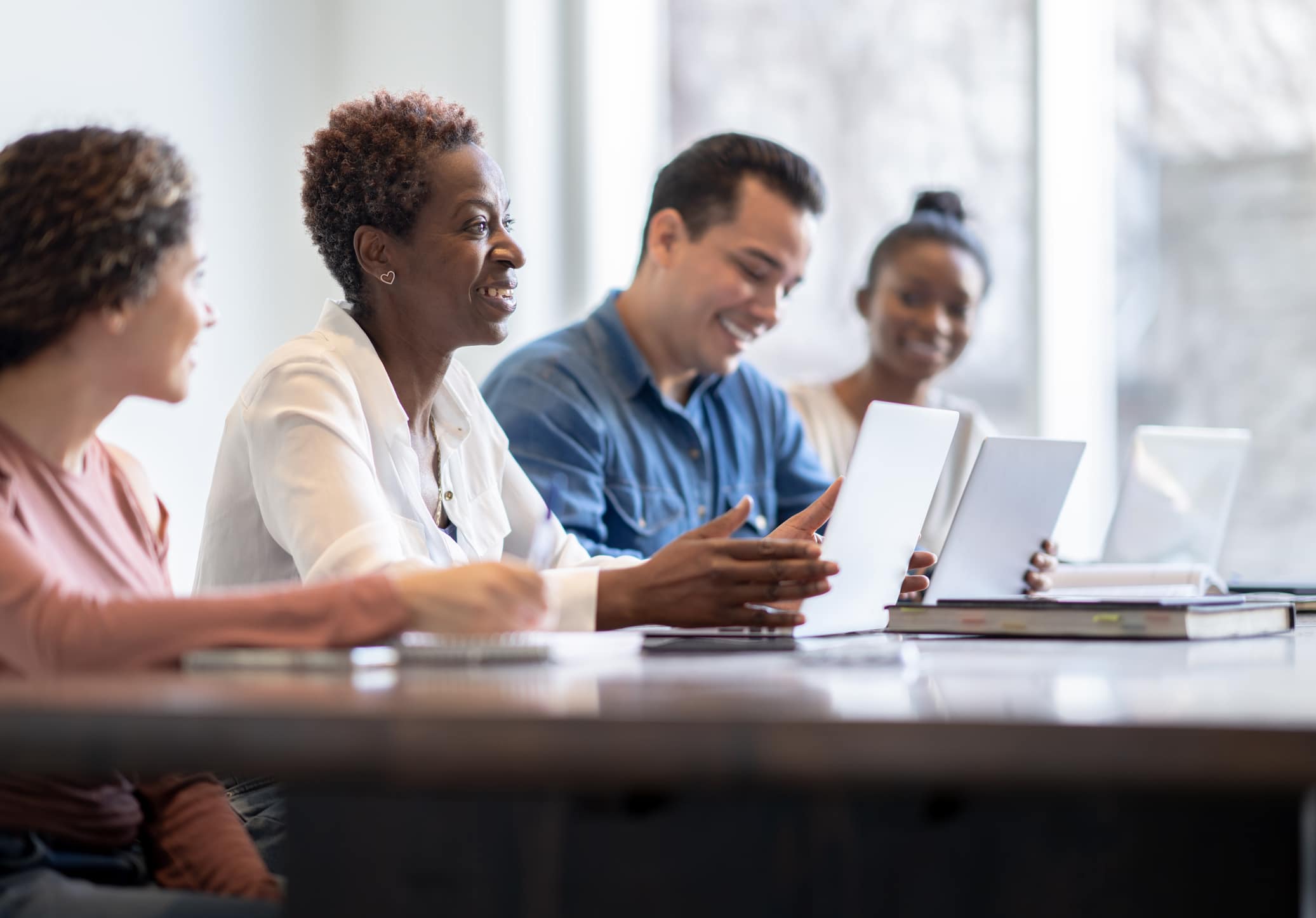 A group of four adults sit together at a table with laptops